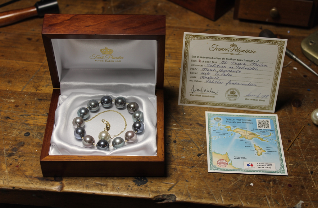 Collier de perles de Tahiti posé sur un écrin en bois avec un certificat de traçabilité manuscrit.