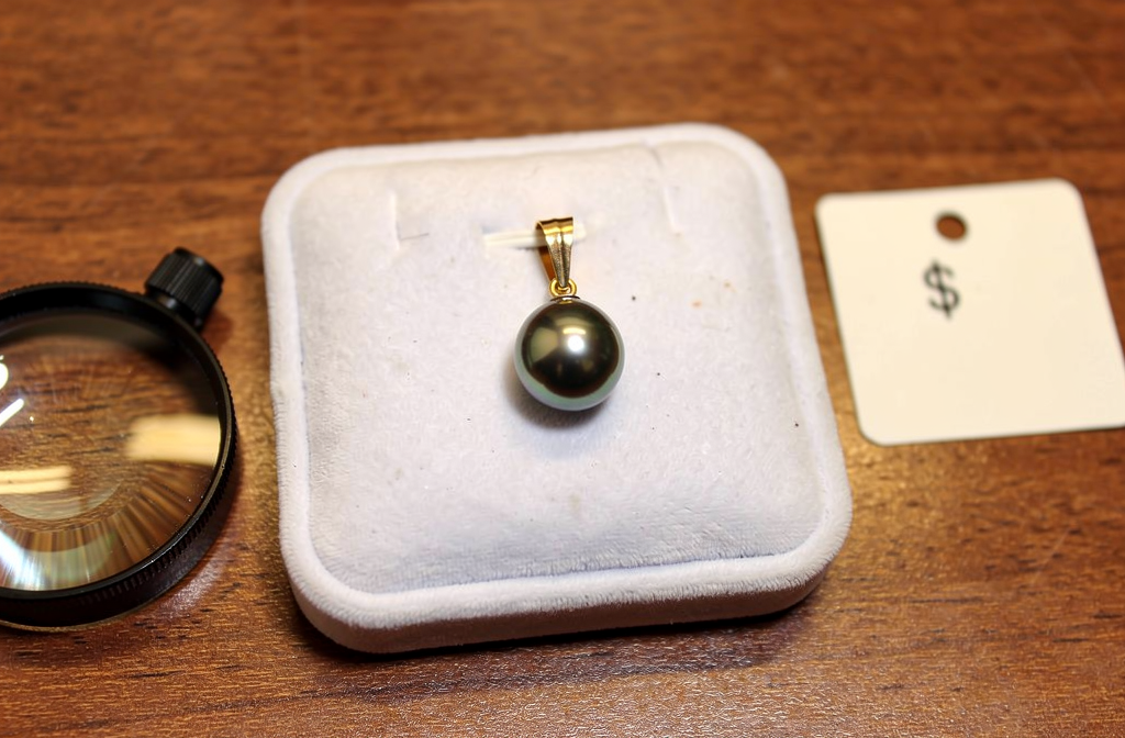 Pendentif perle noire de Tahiti en or posé sur un écrin de velours blanc chez un bijoutier-revendeur.